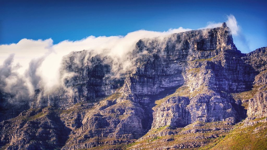 Flat topped rocky mountain with cloud cascading down the sheer slope